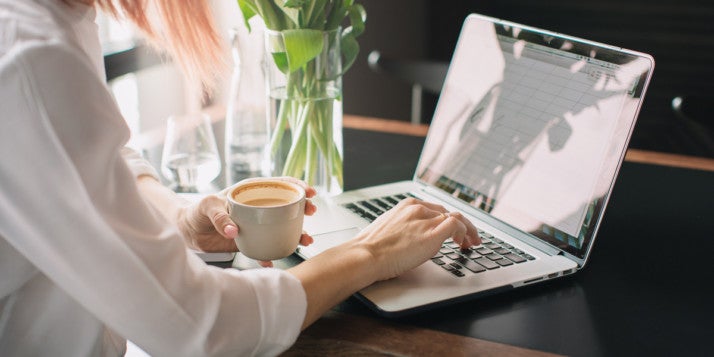 A woman drinking coffee and using a laptop