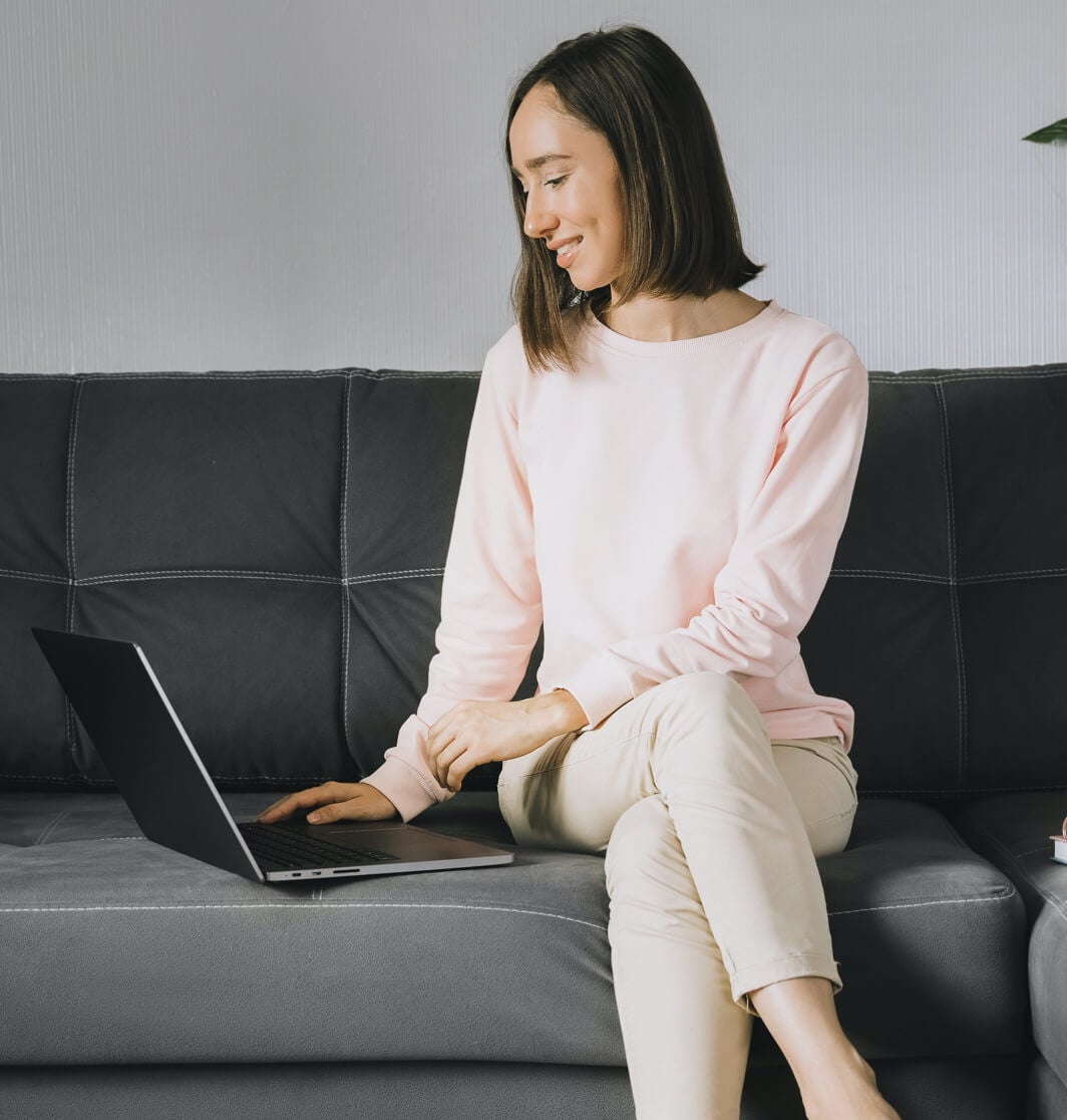 Una donna seduta sul divano lavora al suo curriculum sul suo laptop.