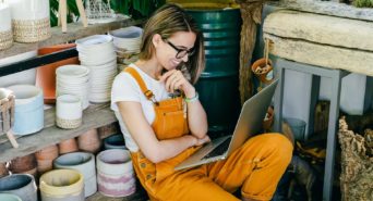 Woman in her pottery studio smiles and she reads from her laptop.